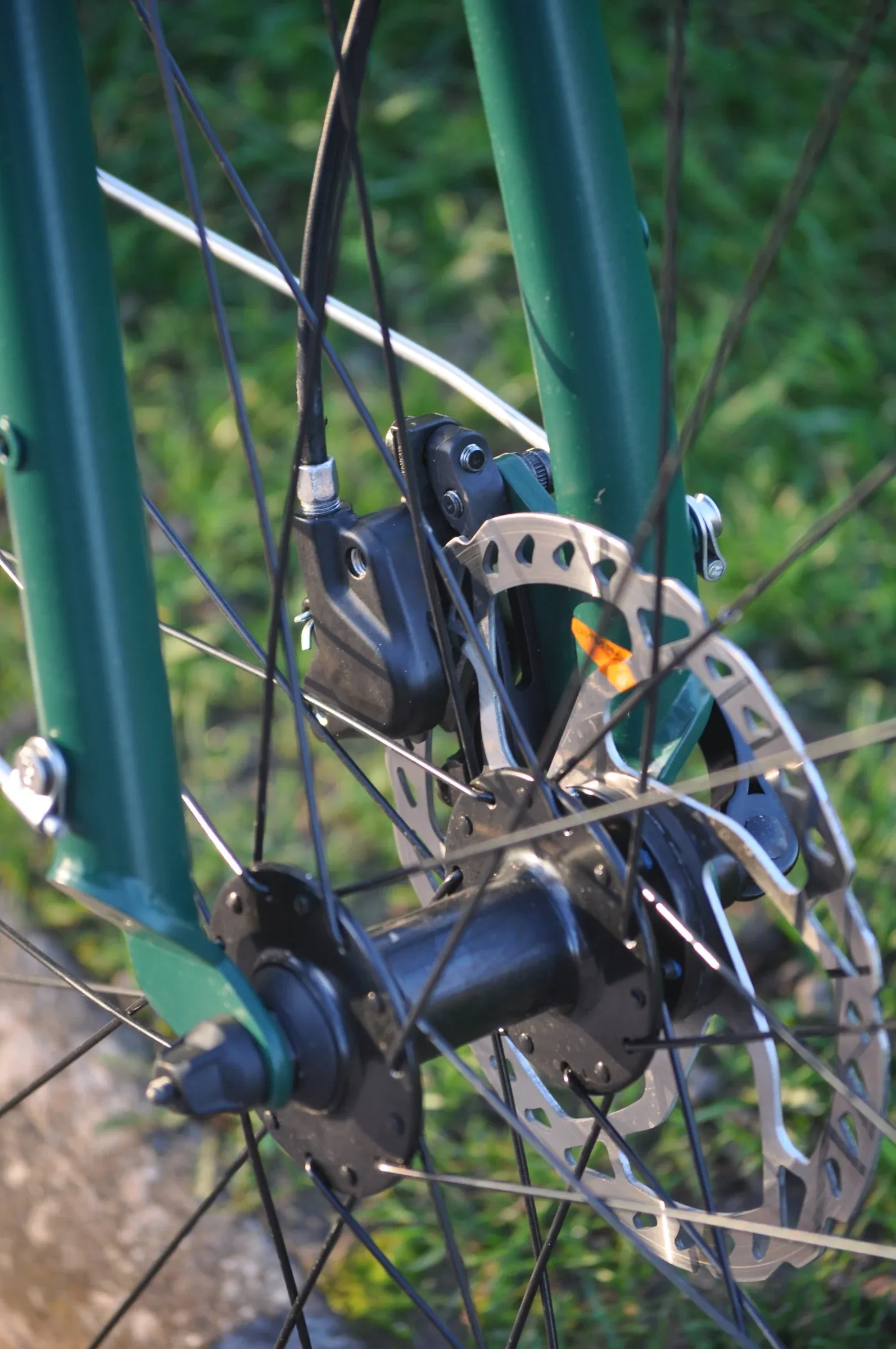 Détail du frein à disque avant d'un vélo urbain vert mousse, avec étrier bleu et disque rotor métallique visible.