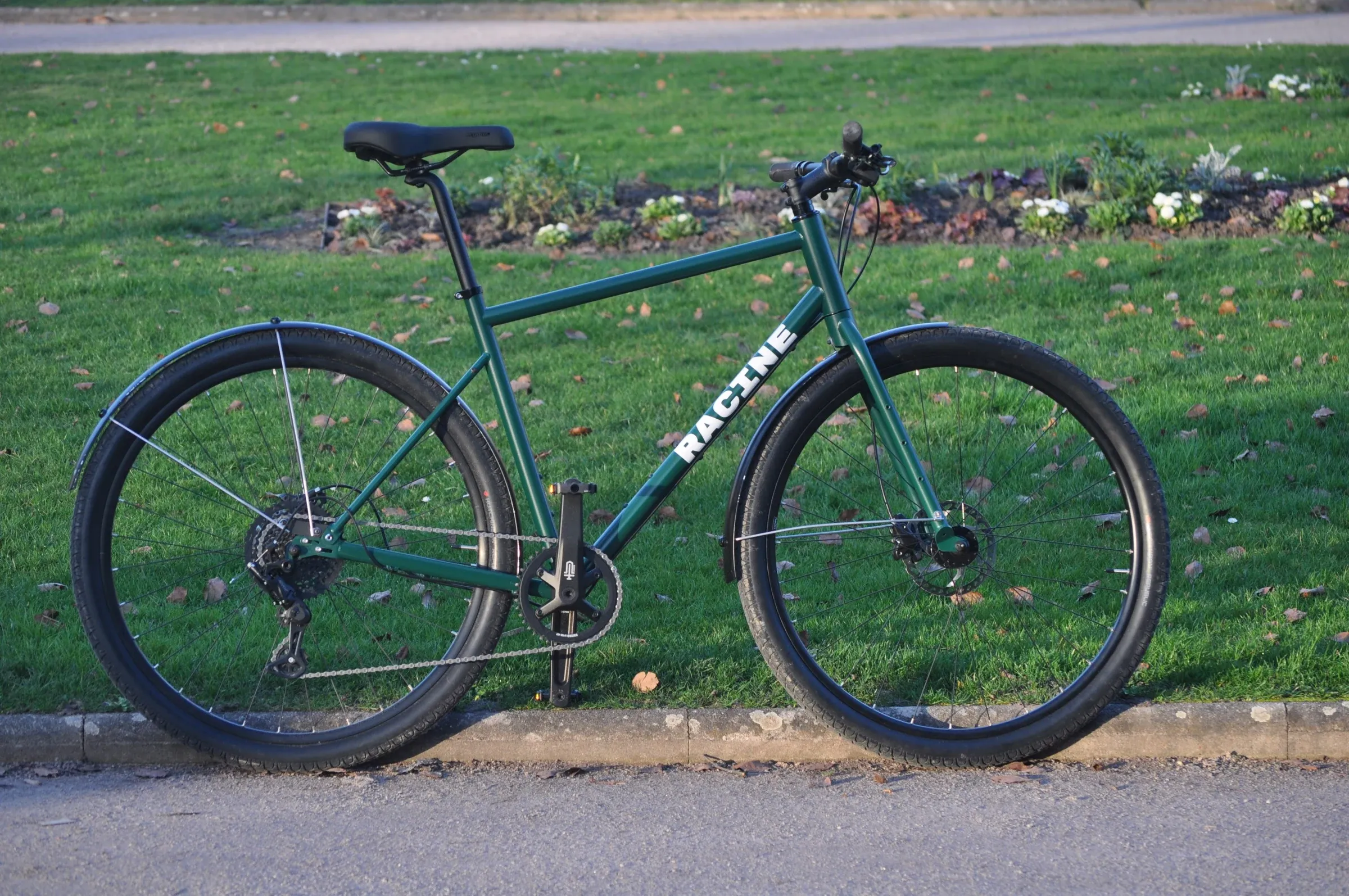 Vélo urbain vert mousse Vélos-Racine posé de profil sur un sentier, parc en arrière-plan