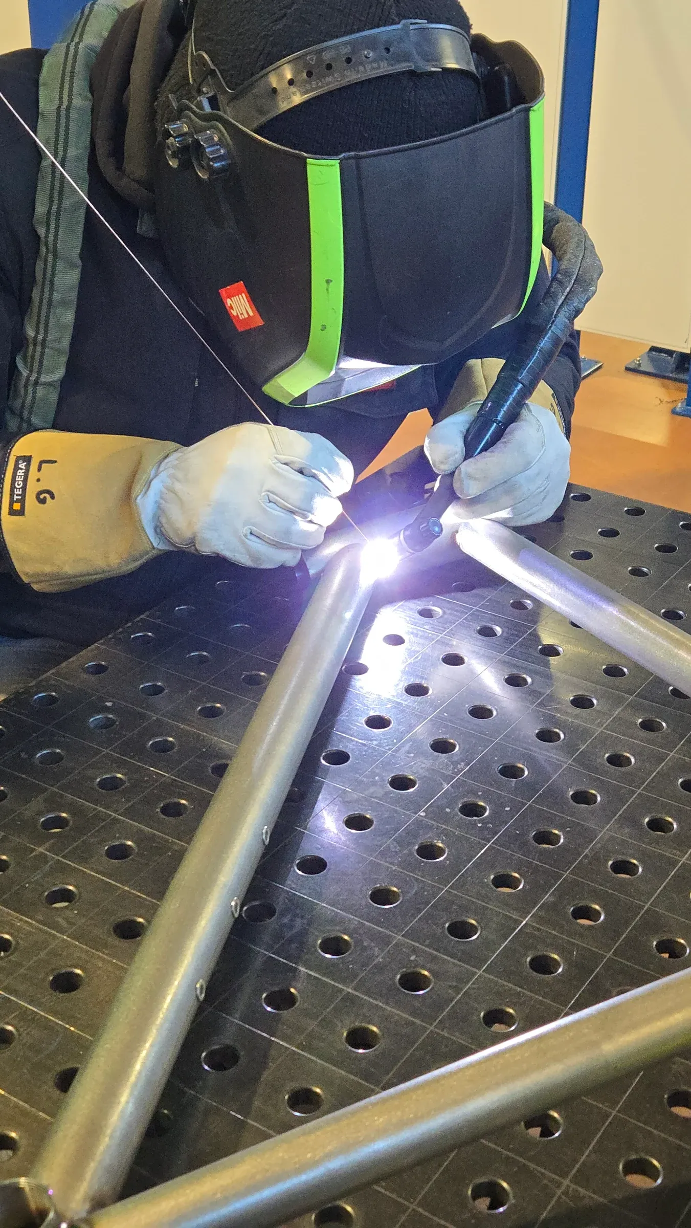 Soudure TIG en cours sur tube de cadre acier, masque de soudeur, atelier industriel